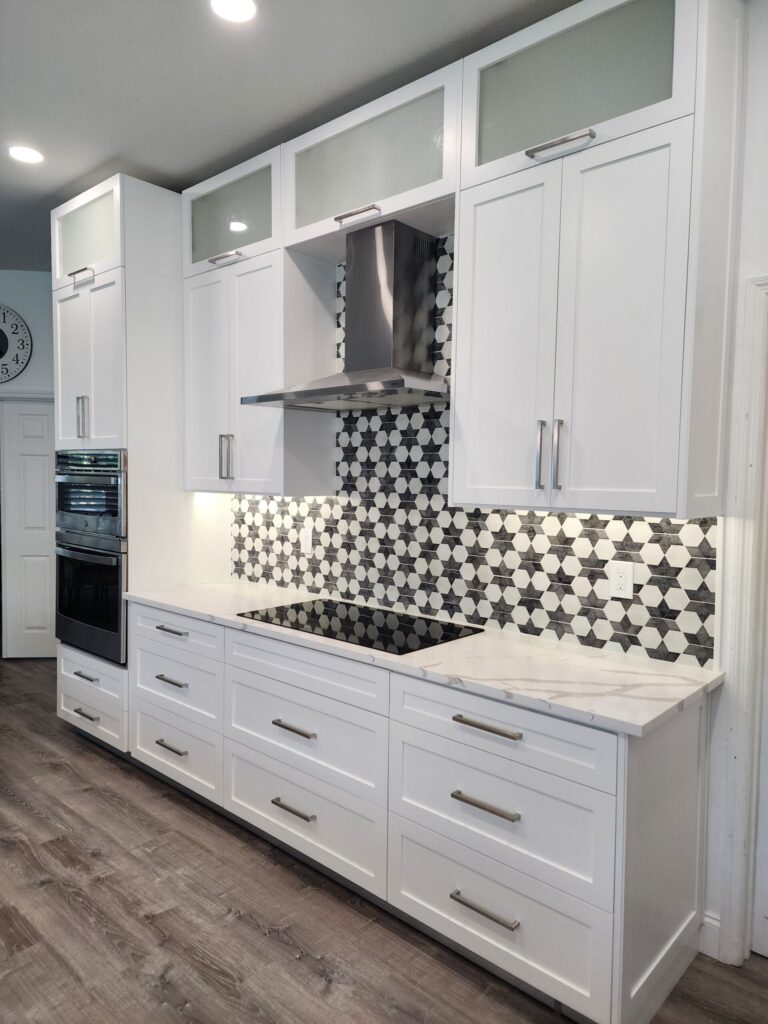 White upper kitchen cabinets surrounding a range hood above a patterned backsplash