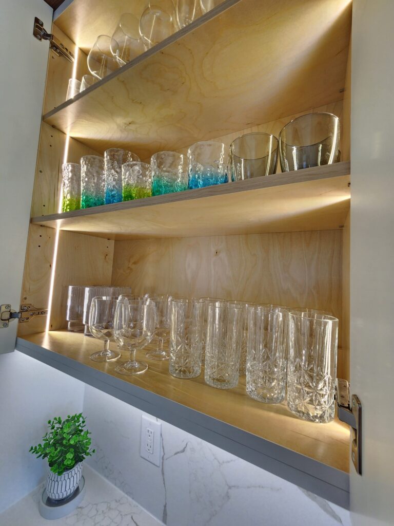 Close-up of illuminated open wood wall cabinet shelves holding glassware