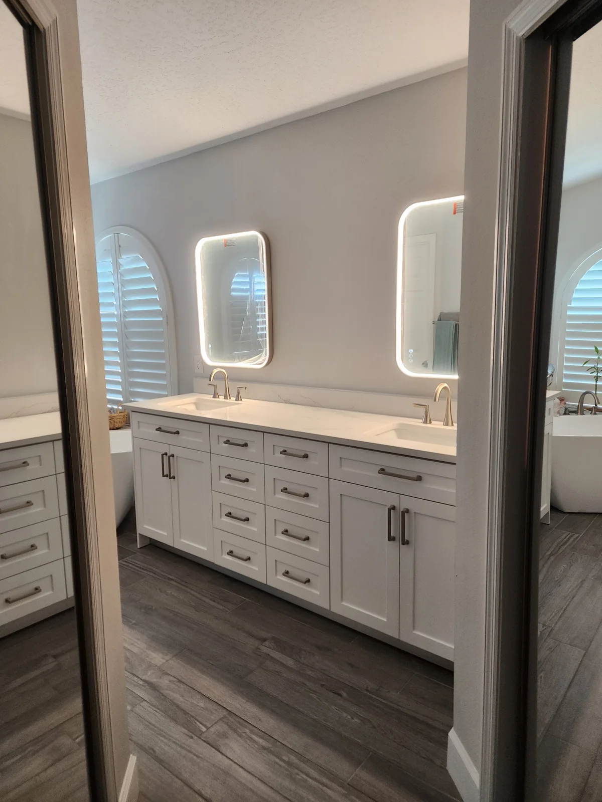 White double-sink vanity with installed cabinet doors and drawers, viewed through a bathroom doorway