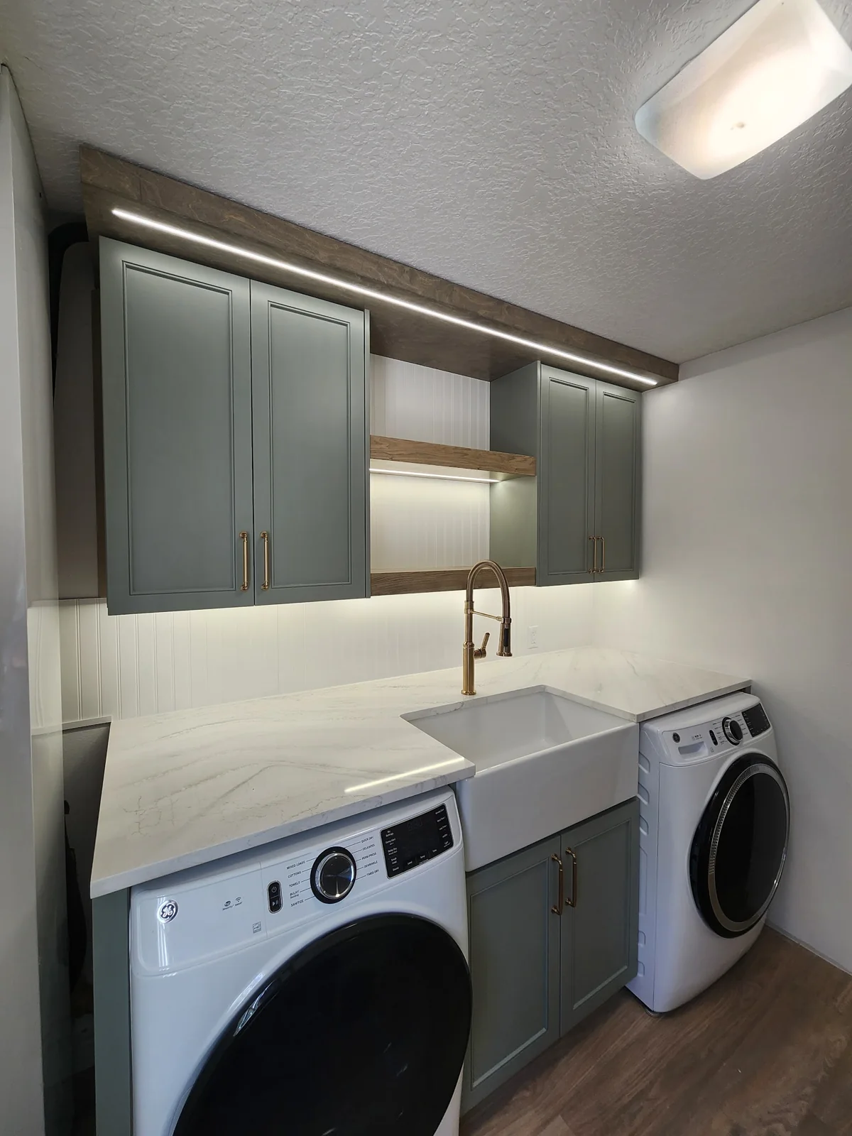 Gray laundry room cabinets with open wood shelving above a sink between a washer and dryer